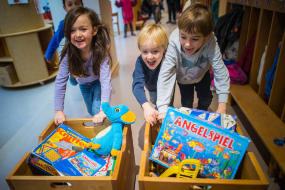 Drei Kinder schieben begeistert Spielzeugkisten durch die Kita.