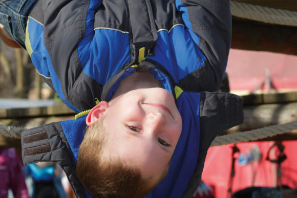 Ein Junge hängt kopfüber am Klettergerüst auf einem Spielplatz.