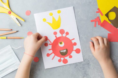 Kinderhände basteln ein Bild, das das Corona-Virus darstellt.