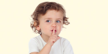Ein kleines Kind hält sich den Zeigefinger an die Lippen und bedeutet so: Ruhe bitte.