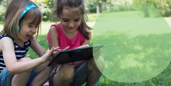 Foto: Zwei Mädchen sind in einem Garten oder Park und gucken zusammen in ein Tablet.