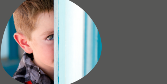 Kleiner Junge im Close-Up schaut hinter einer Tür hervor.