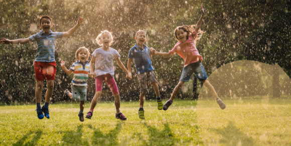 Fünf Kinder zwischen etwa 3 und 6 Jahren springen auf einer Wiese in die Höhe.