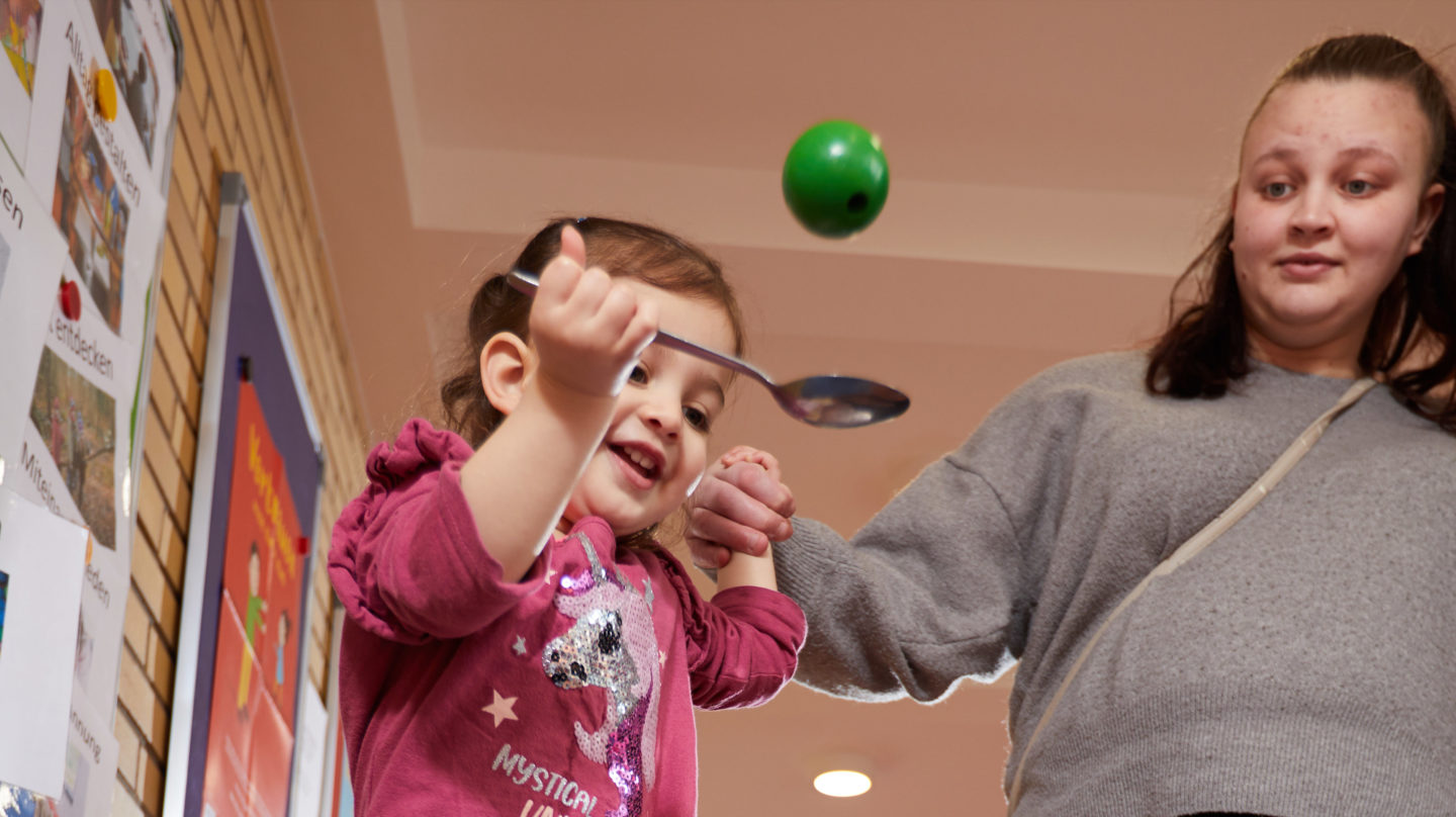 Mutter und Kind spielen Eierlaufen mit einem Ball.