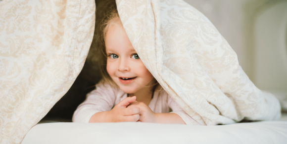 Kleines Mädchen guckt unter einer weißen Decke hervor