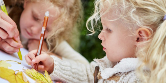 Mädchen malt und bastelt mit Herbstblättern im Kindergarten