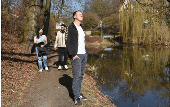Drei Erwachsene gehen in der Pause an einem Teich spazieren.