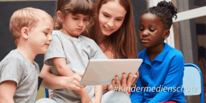 Eine Gruppe von Kindern und einer Betreuerin schaut gemeinsam auf ein Tablet.