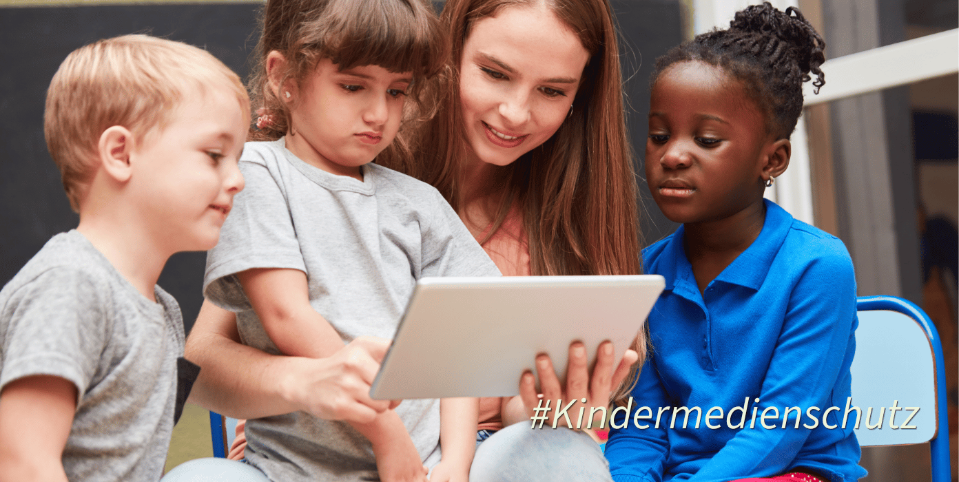 Eine Gruppe von Kindern und einer Betreuerin schaut gemeinsam auf ein Tablet.