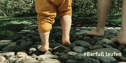 Ein Kleinkind läuft barfuß über einen Steinweg im Freien, umgeben von Natur.