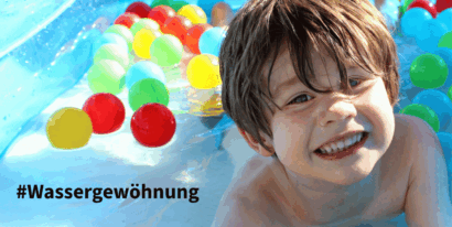 Ein fröhlicher Junge im Wasser mit bunten Bällen, ideal für Wassergewöhnung und Spielspaß.