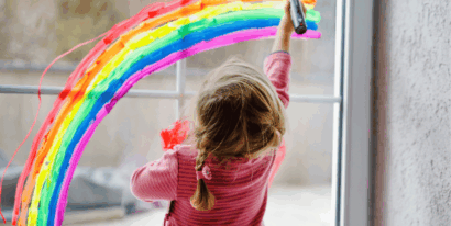 Ein Kind malt einen Regenbogen auf eine Fensterscheibe, was für sichere Fenster und Türen in Kitas wichtig ist.