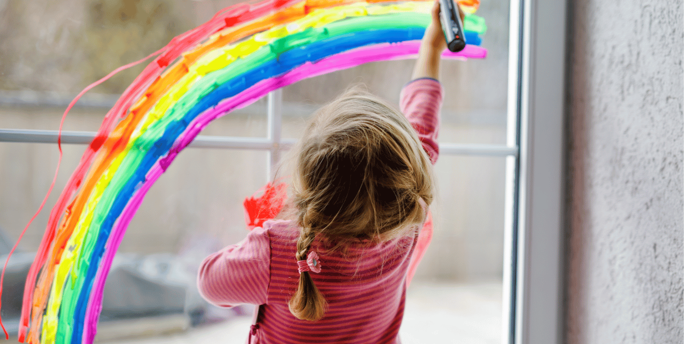 Ein Kind malt einen Regenbogen auf eine Fensterscheibe, was für sichere Fenster und Türen in Kitas wichtig ist.