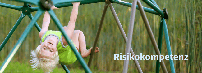 Fokus_Risikokompetenz Ein Kind mit blonden Haaren hängt kopfüber an einem grünen Klettergerüst im Freien. Ein Text spezifiziert das Geschehen: Risikokompetenz.