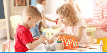 Ein Junge und ein Mädchen spielen konzentriert mit bunten Holzbausteinen und einer Brücke an einem Tisch im Kindergarten.